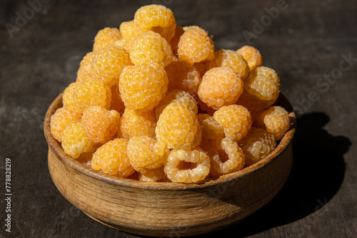 Yellow raspberries in a wooden bowl on the table. Summer berries background. Vitamin food, berry harvest. Healthy nutrition.
