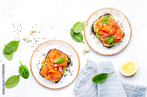 Avocado and salmon toast on rye bread with spinach, cashew and sesame seeds, white table background, top view © 5ph