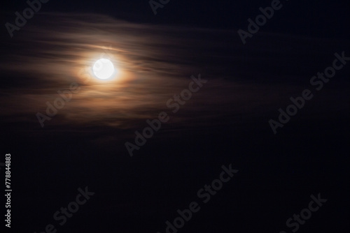 Full moon in the dark night sky with clouds, closeup of photo.Full moon in the dark night sky.