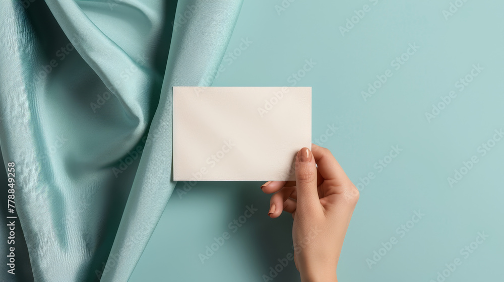 Fototapeta premium Hand holding blank card on teal fabric.