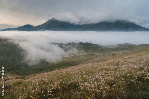 Misty mountains shrouded in fog create a dramatic landscape with a hint of a lake reflecting the cloudy sky