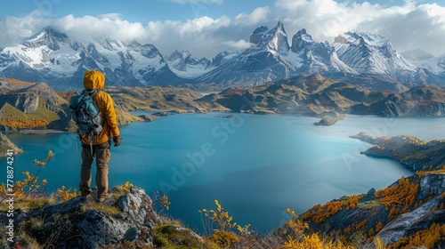  Person standing atop mountain, gazing down at lake surrounded by peaks, with clouds overhead