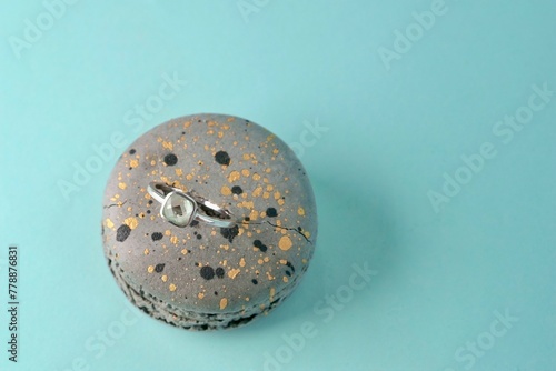 close-up of an engagement silver ring with a gemstone inserted in a grey speckled macaroni cake on an azure background