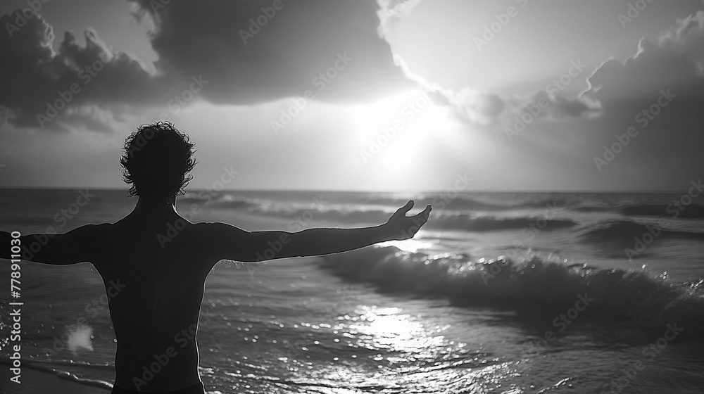 Naklejka premium A man stands with his arms outstretched on the beach sunset, silhouette style, monotone black-white
