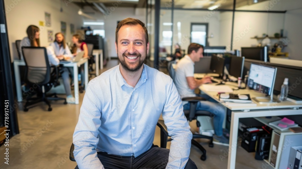 Portrait of a business man sitting in an office with his colleagues in the background. Happy business man working in a co-working office. Portrait of a business man sitting in an office with his colleagues in the background. Happy business man working in a co-working office.