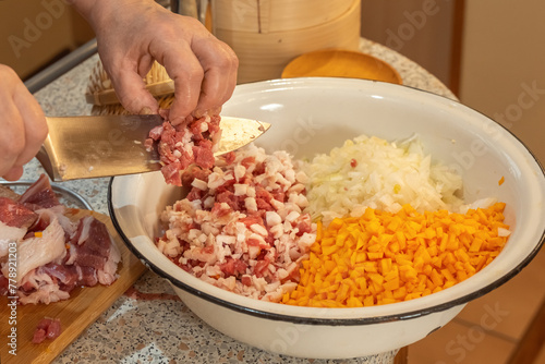 Cook pours finely chopped meat from a knife into a bowl with chopped onions and pumpkin to prepare minced meat.