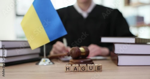 Word hague is written on wooden cubes near flag of ukraine and judge in courtroom closeup 4k movie slow motion. International court of justice punishment for war crimes concept photo