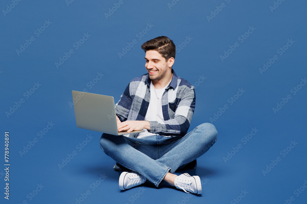 Full body smart young IT man he wear shirt white t-shirt casual clothes sit hold use work on laptop pc computer chat online isolated on plain blue cyan background studio portrait. Lifestyle concept.
