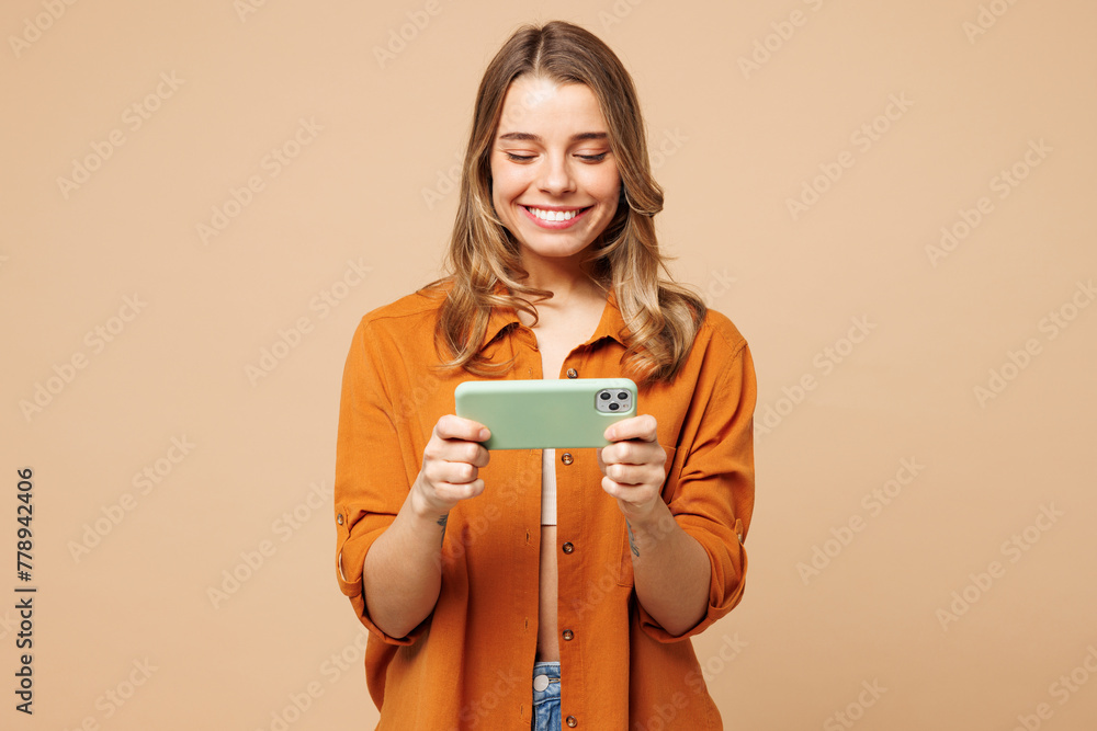 Young gambling woman wear orange shirt casual clothes use play racing app on mobile cell phone hold gadget smartphone for pc video games isolated on plain light beige background. Lifestyle concept. Young gambling woman wear orange shirt casual clothes use play racing app on mobile cell phone hold gadget smartphone for pc video games isolated on plain light beige background. Lifestyle concept.
