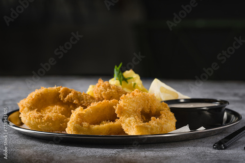 Fried calamari with potato salad next to it on stone table