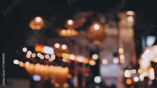 Beautiful bokeh in a dark blurry background at night on the walking street with the people. The round colorful bokeh shine from buildings and shops in the city lifestyle. Abstract concept.