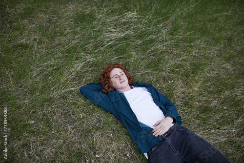 Red-haired man relaxing on grass, serene in nature
