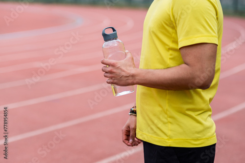 athlete man takes a moment to catch his breath on the running track, holding refreshing water bottle at the city sports arena. 