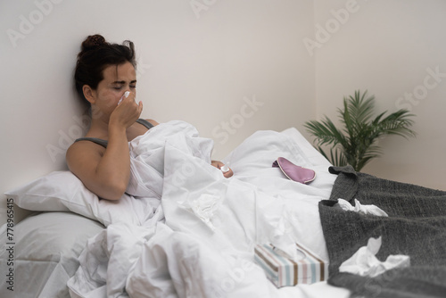A sick woman, tissues in hand, holds medical drops in bed, fighting her illness. 