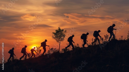A group of people are hiking up a hill, with the sun setting in the background. The silhouettes of the hikers create a sense of unity and camaraderie