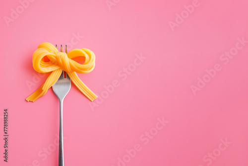 A bow made with pasta on fork. Swirl of spaghetti shaped as a bow. Pasta love, Italian cuisine. Copy space, design element for menu for Italian restaurant, pasta bar. Creative food love concept photo