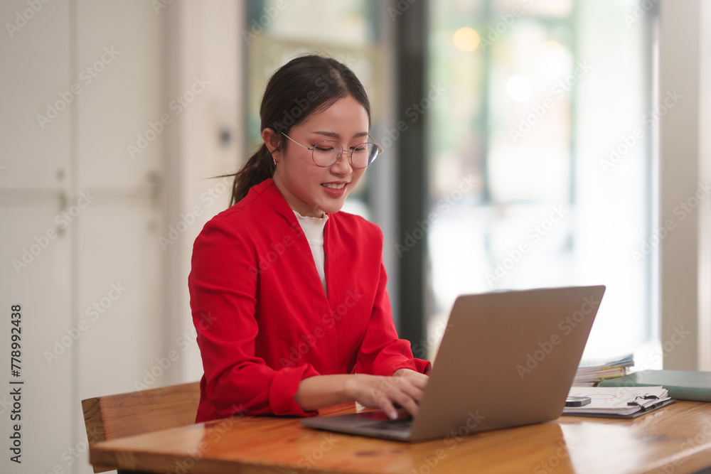 Asian businesswoman in a red jacket is sitting at a table with a laptop in front of her Asian businesswoman in a red jacket is sitting at a table with a laptop in front of her