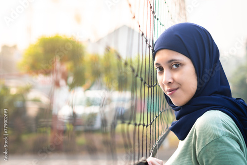 Muslim woman in hijab with brown eyes holding volleyball net in morning sunlight. photo