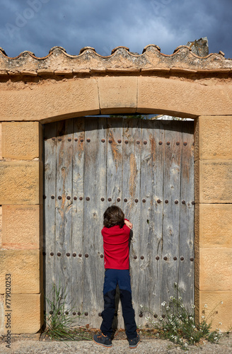 Niño cuenta de espaldas, frente a una vieja puerta de madera, para iniciar el juego del escondite en el pueblo de Fuentespalda, Teruel (Aragón), España.