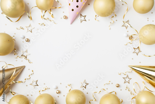Fashion birthday party festive background with golden decoration from balloons, carnival cap and confetti stars on white table top view. © juliasudnitskaya