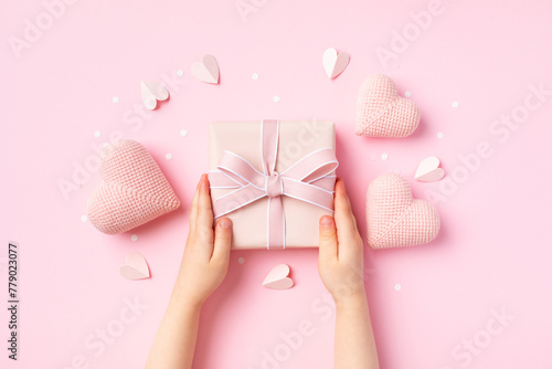Child hands holding a gift or present box decorated with pink hearts for Happy mothers day. Holiday greeting card.
