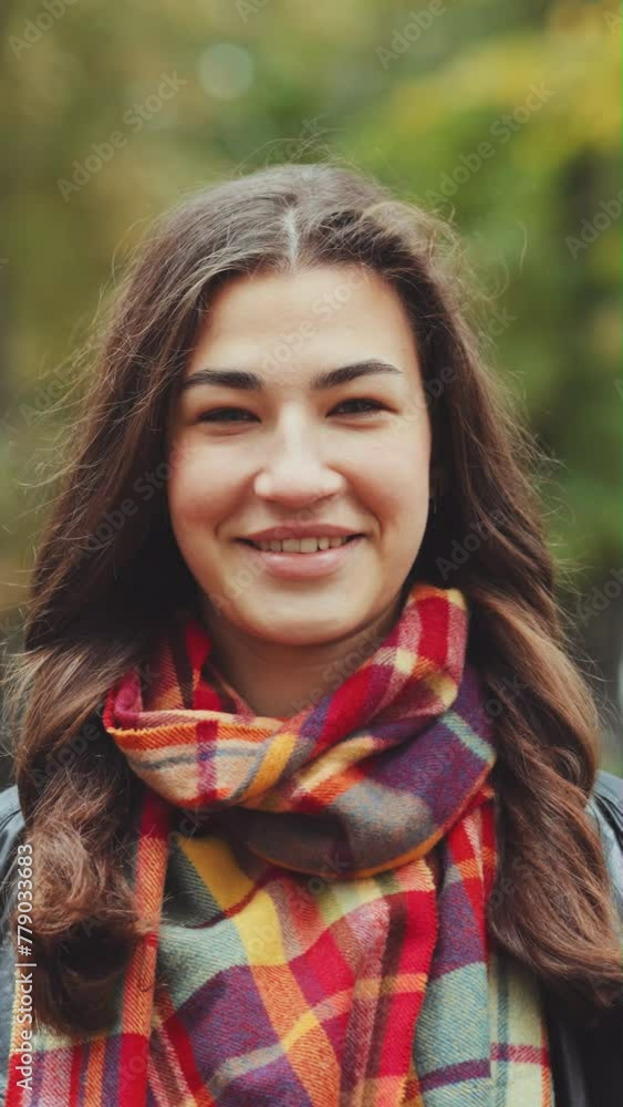 Vertical Screen: Young woman with long hair wearing leather jacket with checkered scarf standing in windy autumn park and smiling at camera. Portrait of happy person. Concept of emotion Vertical Screen: Young woman with long hair wearing leather jacket with checkered scarf standing in windy autumn park and smiling at camera. Portrait of happy person. Concept of emotion