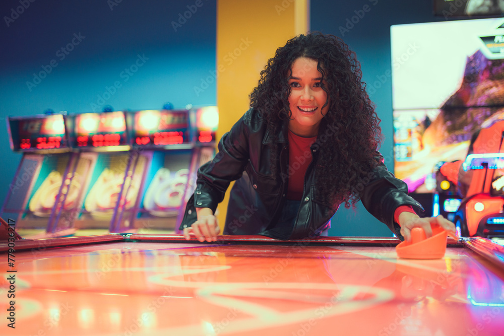 Fototapeta premium Excited young woman enjoying an air hockey game at a vibrant arcade