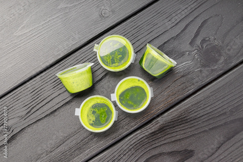 Three cups of wheatgrass juice, top view on a dark wooden table.