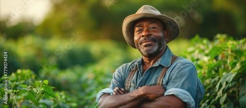 An African American gardener in a hat standing confidently with his arms crossed in a vast field.