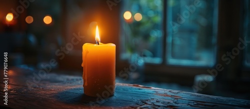 A lit candle sits on top of a wooden table, casting a warm glow in the surroundings.