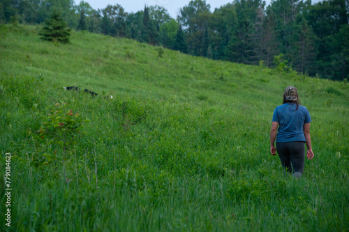 A woman walks with her border collie dog in a field in the summer