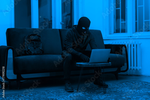 Masked hacker using laptop in dark room © Prostock-studio