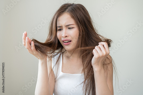 Damaged Hair, frustrated asian young woman, girl hand in holding splitting ends, messy unbrushed dry hair with face shock, long disheveled hair, health care of beauty. Portrait isolated on background.