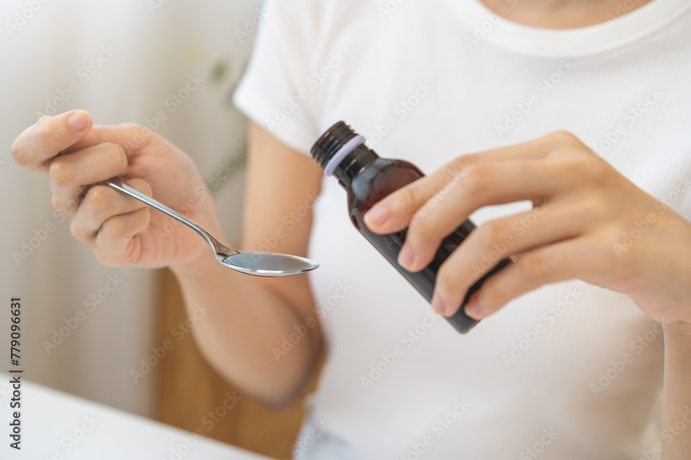 Close up hand of sick woman pouring syrup, liquid antipyretic, cough, flu medicine to stainless spoon from bottle, measuring dosage of drug with tablespoon, taking therapy, treatment cure of disease.