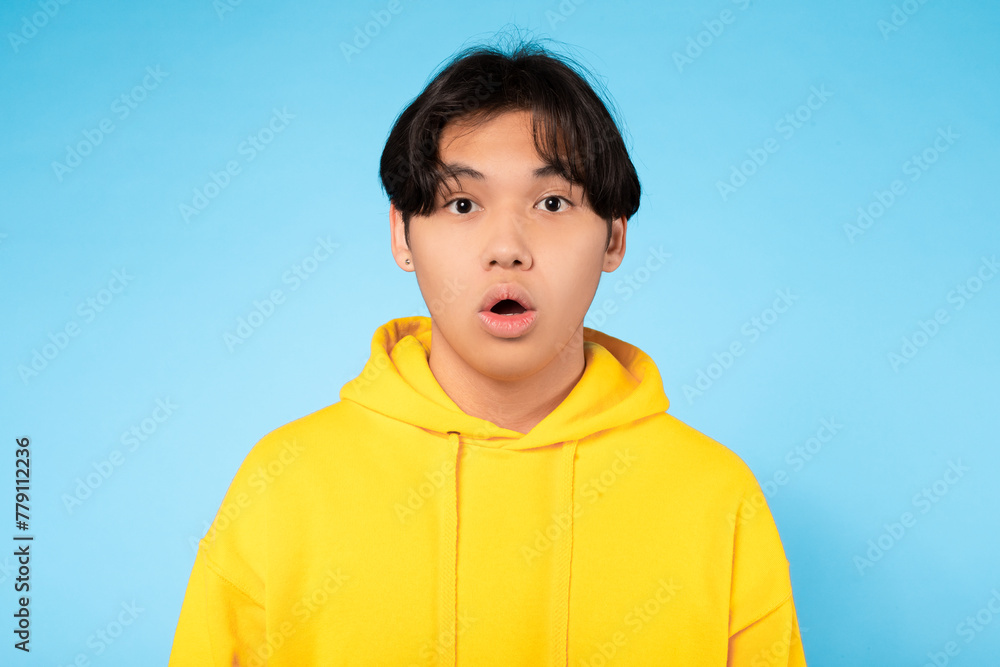 Surprised guy in yellow hoodie, close-up, blue background Surprised guy in yellow hoodie, close-up, blue background