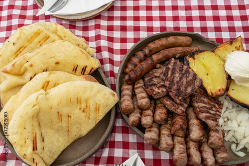 Fototapeta Naklejka Na Ścianę i Meble -  Mixed platter of meat with Cevapcici, sausages and pleskavica served in local restaurant in Maribor, Slovenia. Served with potatoes, onions and pita bread. National dish in traditional shop