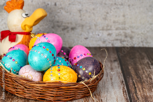 Decorated colorful Easter eggs in a basket and a funny blurred gypsum chicken in the background