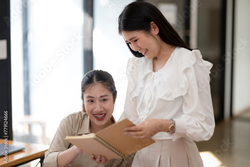 Two female colleagues discuss and review documents together in a bright office, working collaboratively on a business project.