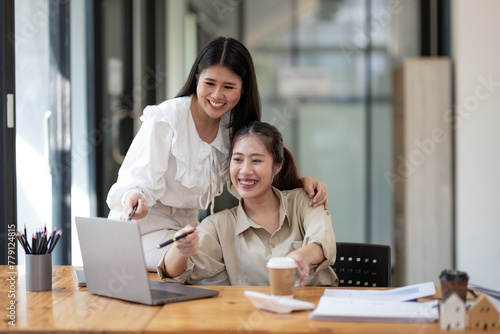 Two female colleagues collaboratively working on a project with a laptop in a bright office space.