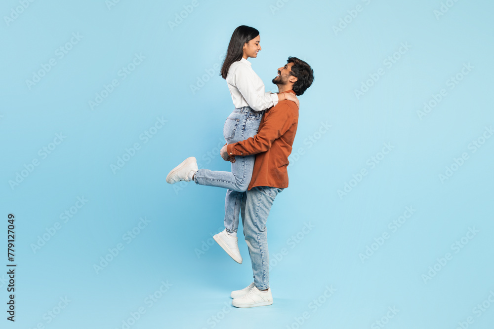 Man lifting woman on blue background in joyful pose Man lifting woman on blue background in joyful pose