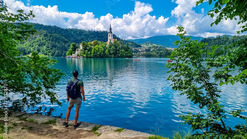 Tourist man with panoramic view of St Mary Church build on small island on alpine lake Bled, Upper Carniola, Slovenia. Serene landscape in Julian Alps in winter. Hills covered with lush green forest photo