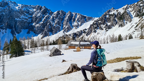 Hiker woman sitting on trunk on Ogrisalm enjoying scenic view of Karawanks mountains in Carinthia, Austria. Looking at snow capped summit of Vertatscha and Hochstuhl. Remote alpine cottage in Bodental photo