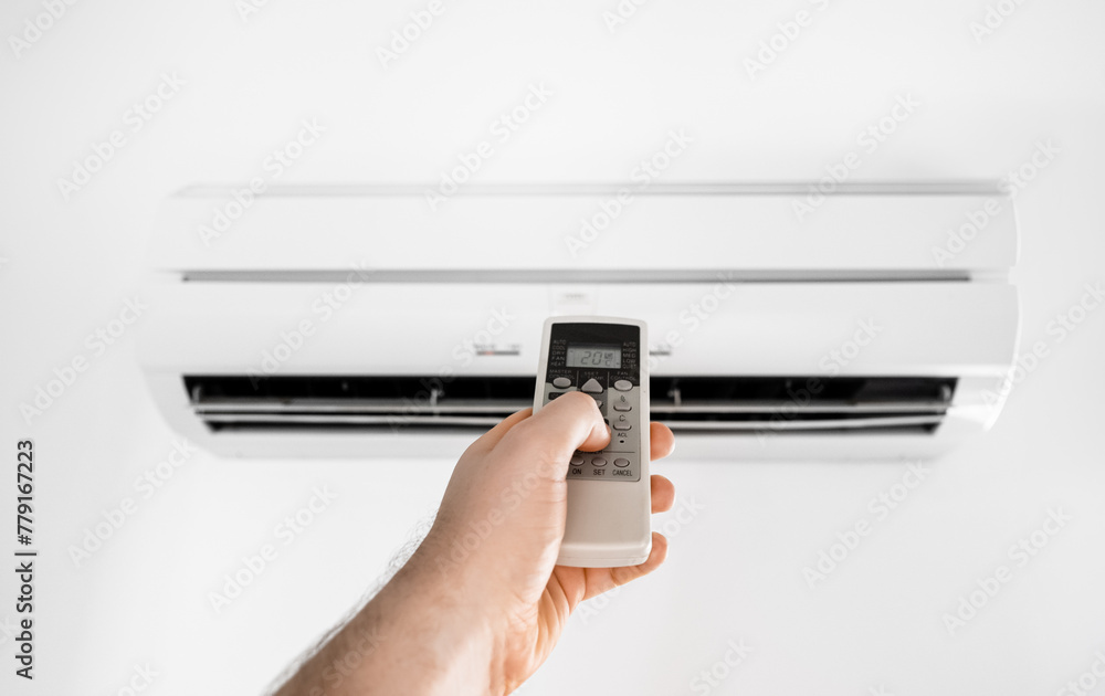 Hand holding remote control in front of the air conditioner.
