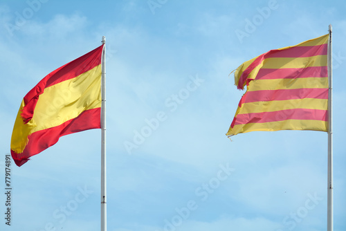 The image captures a moment of peaceful coexistence, with the flags of Catalonia and Spain waving together under a clear blue sky, reflecting cultural and political diversity.