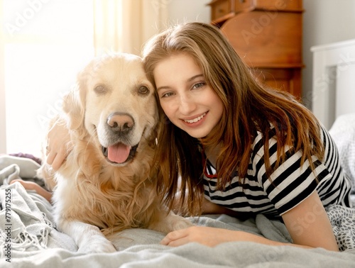 Pretty girl hugging golden retriever dog and smiling sitting in bed. Female teenager with purebred doggy pet labrador looking at camera at home