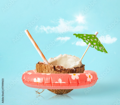 Half of a coconut with ring float, sun umbrella and cocktail straw on a blue background. Creative concept summer beach holiday