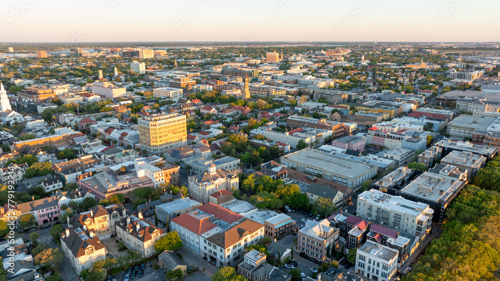 Naklejka premium Golden sunrise light bathes downtown Charleston, South Carolina, with historic buildings and streets visible from an aerial view.