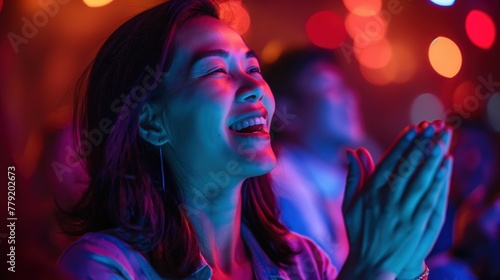 An Asian woman standing with eyes closed, clapping her hands