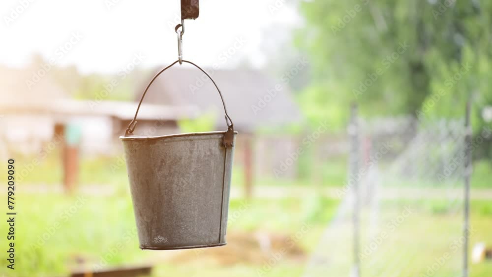 Old metal bucket swinging in the wind around the well in the village yard. Old metal bucket swinging in the wind around the well in the village yard.