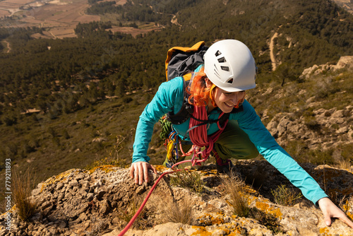 A woman is climbing a mountain wearing a helmet and a blue jacket. She is smiling and she is enjoying the climb